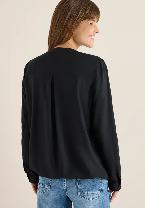 Frau mit langen Haaren trägt schwarze Bluse und Jeans, Blick über die Schulter.
